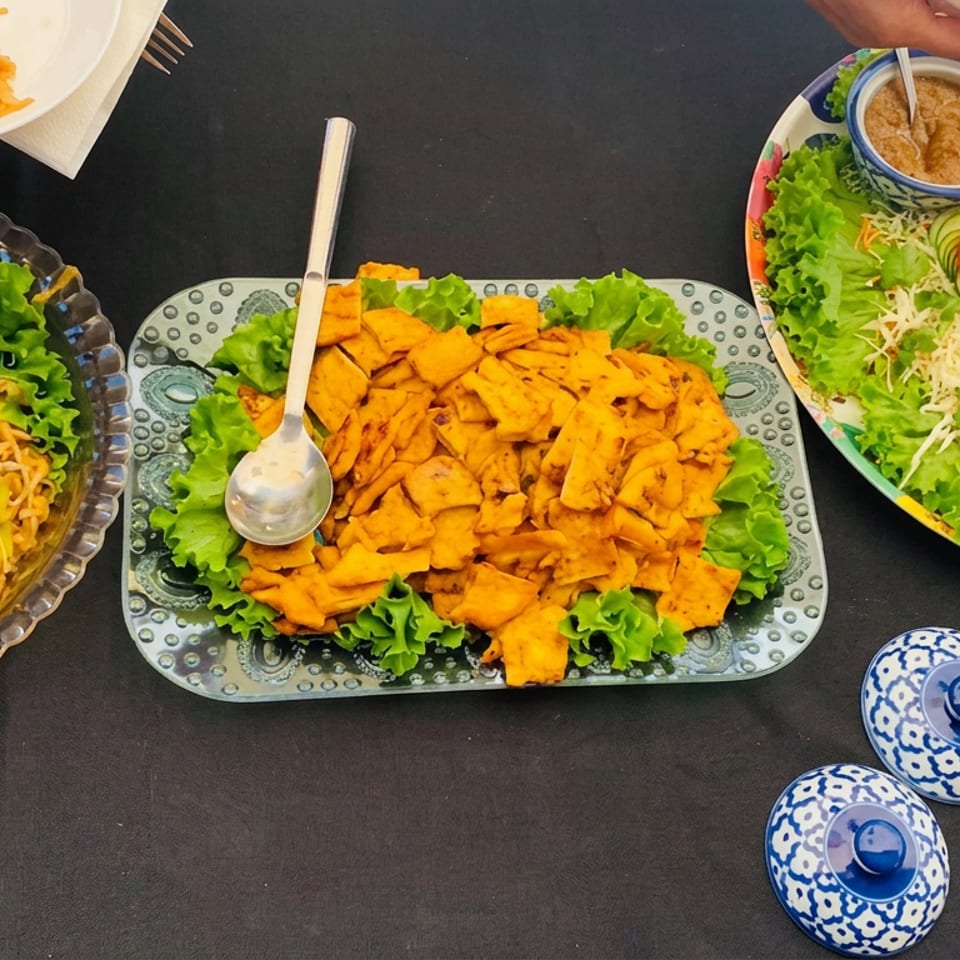 Overhead view of a shared meal featuring spiced rice, fried appetizers, salad with tomato roses, sauces, and blue-and-white condiment bowls.