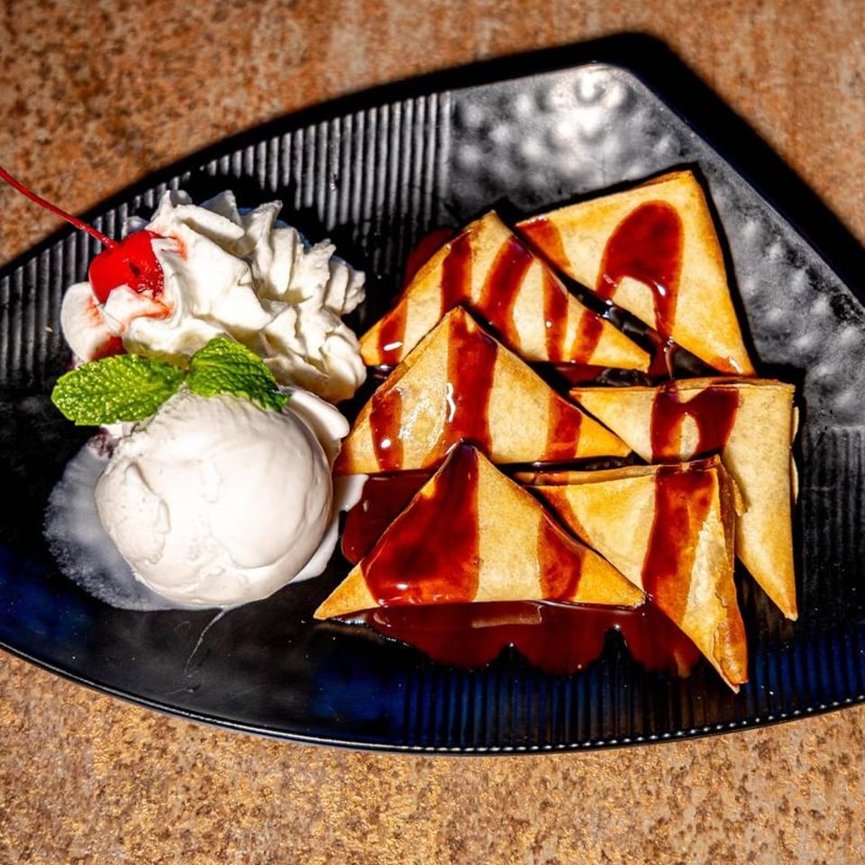 Crispy triangular pastries drizzled with chocolate sauce, served with vanilla ice cream, whipped cream, mint, and a cherry.