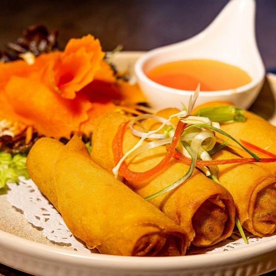 Plate of golden fried spring rolls garnished with shredded vegetables, lettuce, edible flowers, and a bowl of dipping sauce.