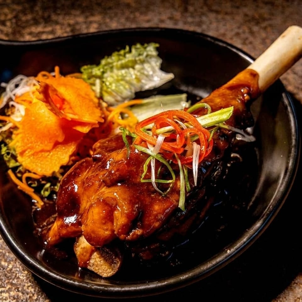 Glazed roasted meat with shredded vegetables and carrot ribbons served in a black bowl with a wooden-handled spoon.